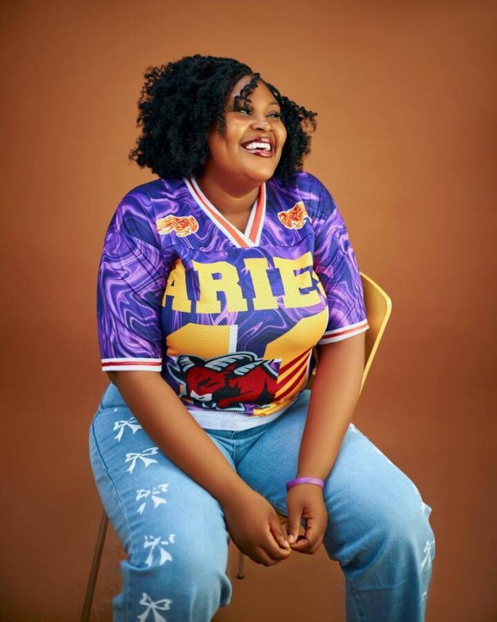 Cheerful woman wearing a vibrant Aries themed jersey sitting on a chair.