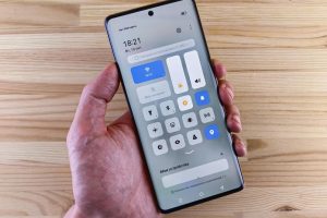 A hand holding a smartphone displaying the control center against a wooden backdrop.