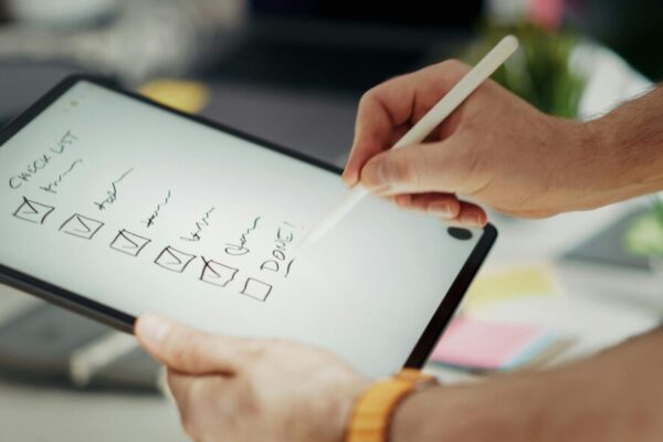 Close-up of a hand writing on a digital checklist using a stylus on a tablet