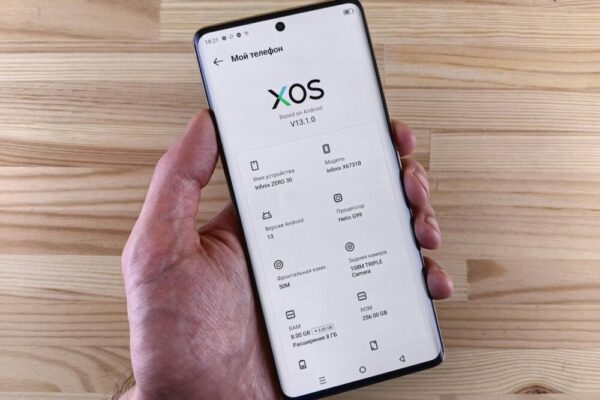 Close-up of a hand holding a smartphone displaying the XOS interface with specs.