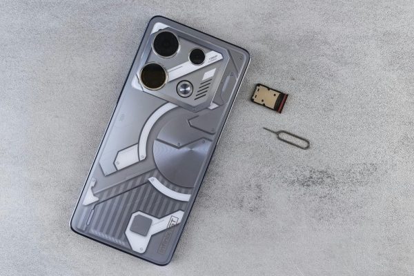 手機死訊號/無服務速查:區域測試與SIM卡卡槽教學 Close-up of a smartphone with futuristic design alongside a SIM card and ejector tool on a gray surface.