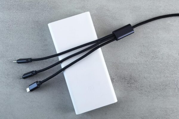 A sleek white power bank with a black multi-connector cable laid on a textured grey surface