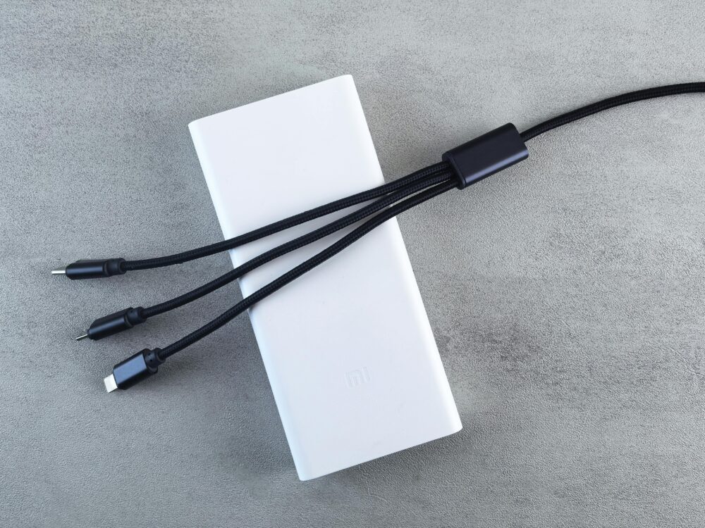 A sleek white power bank with a black multi-connector cable laid on a textured grey surface