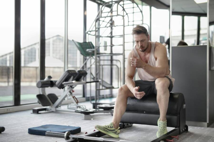 Muscular man sitting on bench in gym, reflecting after workout. Fitness and health concept.