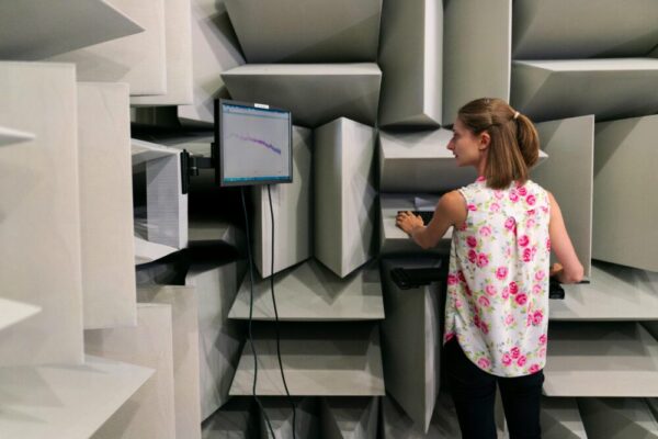 Female engineer testing sound waves in an anechoic chamber with a monitor.