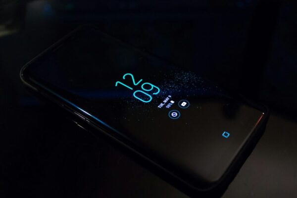 image: Close-up of a smartphone in the dark displaying digital clock and notifications
