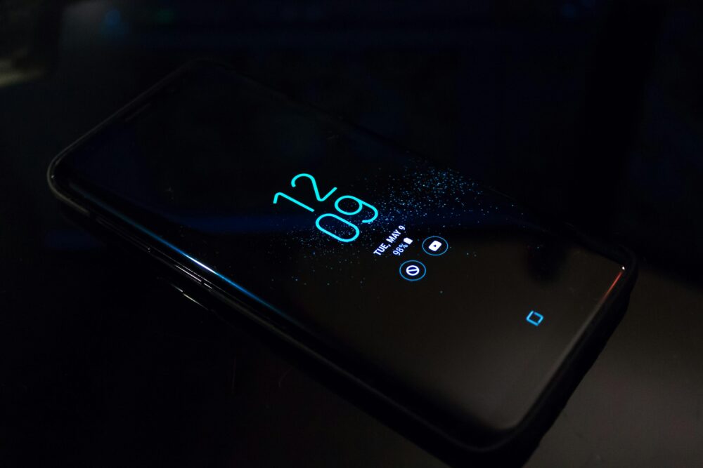 Close-up of a smartphone in the dark displaying digital clock and notifications.