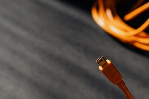 Macro shot of an orange USB cable connector on a textured surface with soft shadows.