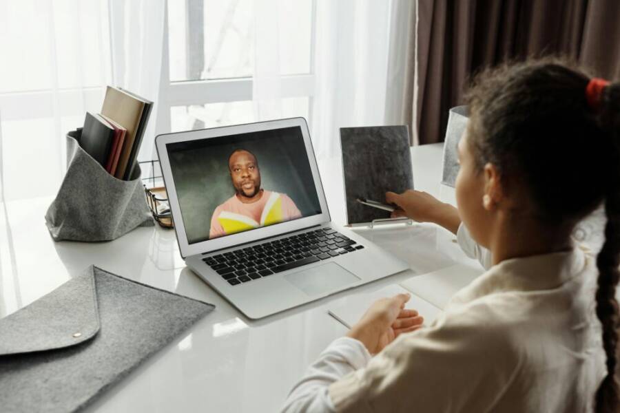A young girl participates in an interactive online class with a teacher on a laptop, fostering education from home.