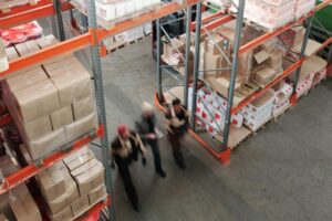 A high angle view of workers in motion in a busy warehouse with shelves full of boxes and packages.