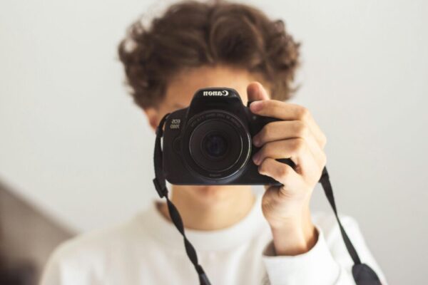 A young adult holding a Canon DSLR camera, capturing a portrait close-up.