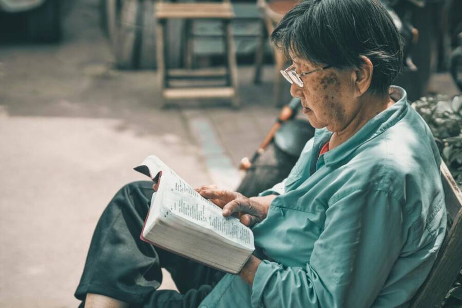 Senior man reading a book outdoors in Beijing, conveying a peaceful and studious atmosphere.