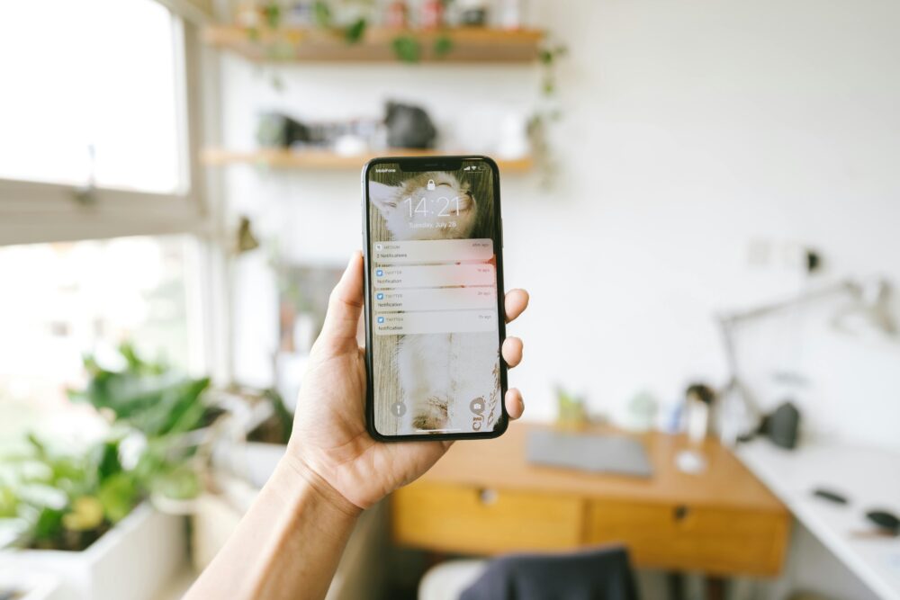 Hand holding smartphone indoors with blurred office background, focus on screen notifications.