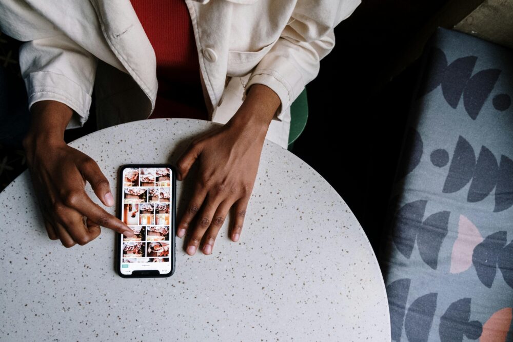 Overhead view of a person browsing photos on a smartphone at a cafe table with a touchscreen