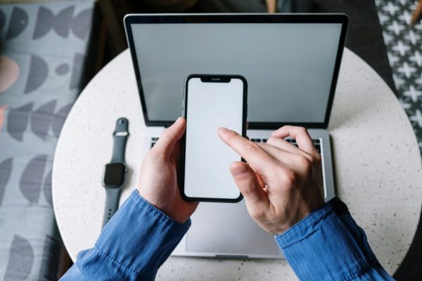 手機觸控回報率與刷新率設定指南:省電流暢的最佳平衡 Hands operating a smartphone above a laptop with a smartwatch nearby, showcasing modern technology.