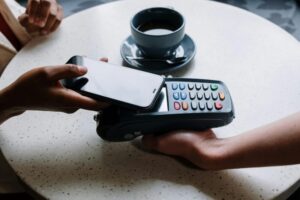 A person using a smartphone to make a contactless payment with a card reader on a cafe table