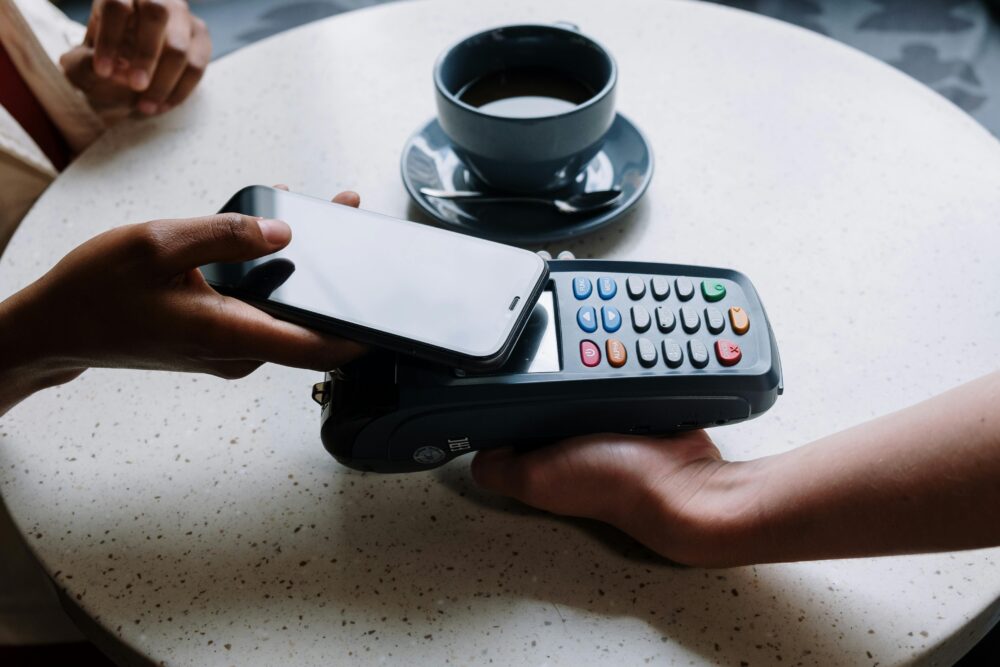 A person using a smartphone to make a contactless payment with a card reader on a cafe table