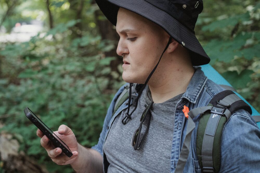 A young man in a forest, using a smartphone to navigate his surroundings.