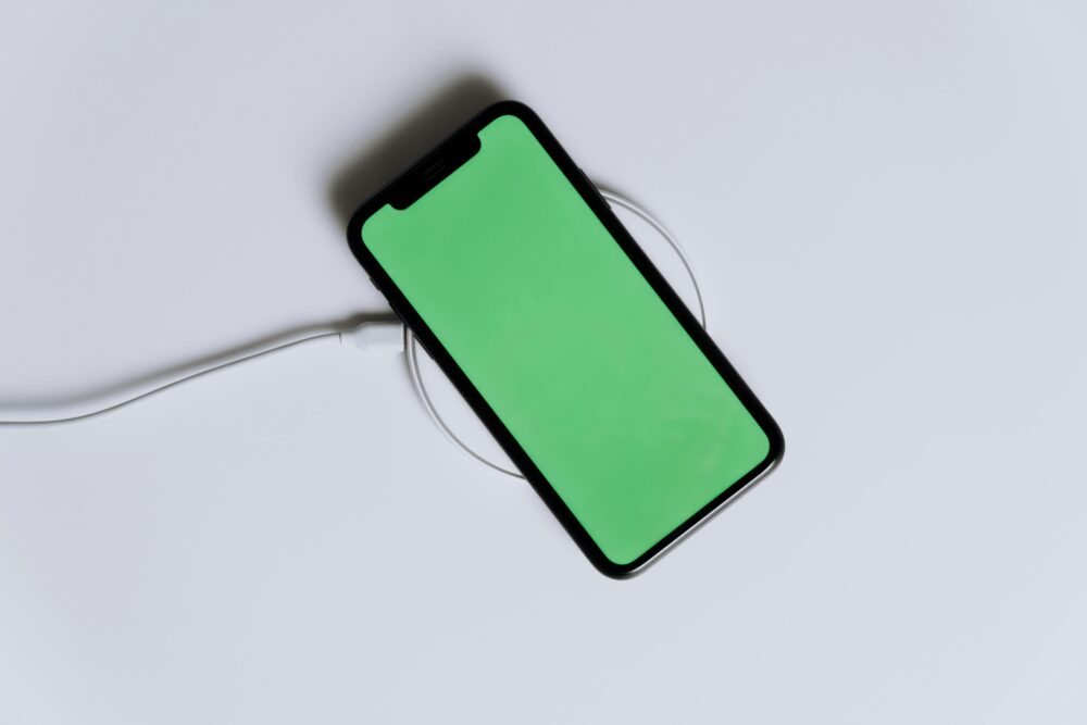 A minimalist smartphone with a green screen on a wireless charger, ideal for tech mockups
