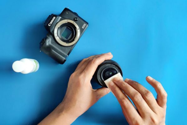 Close-up of hands cleaning a camera lens on a blue surface.