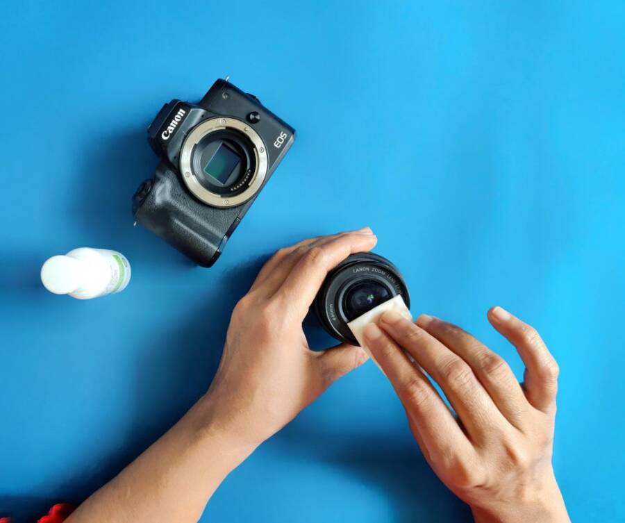 Close-up of hands cleaning a camera lens on a blue surface.