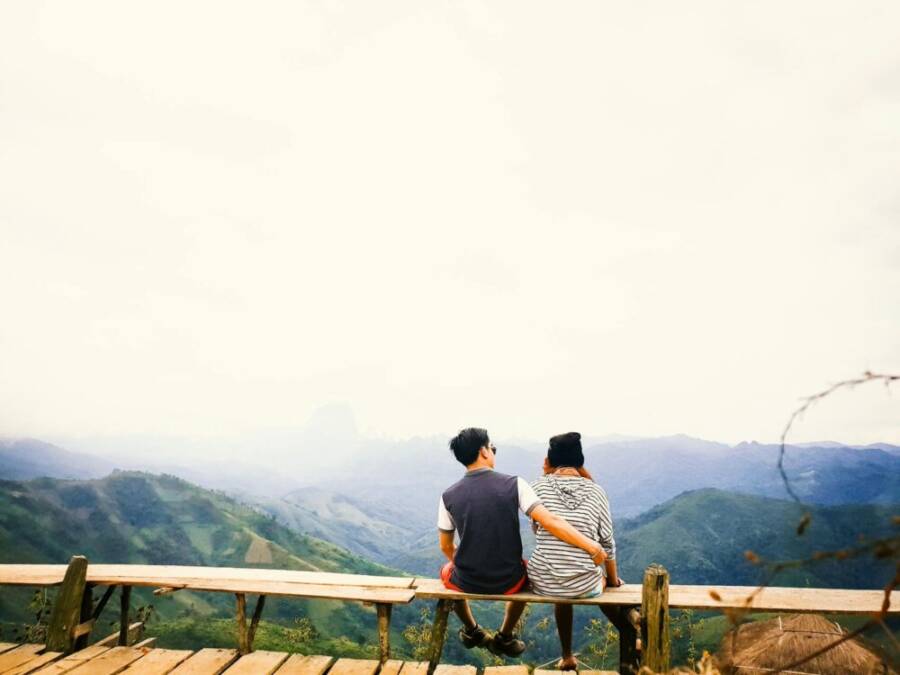 A couple sits on a bench, embracing while overlooking misty mountains in Laos.