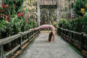 A woman in a backbend yoga pose surrounded by vibrant flowers in a serene outdoor garden.