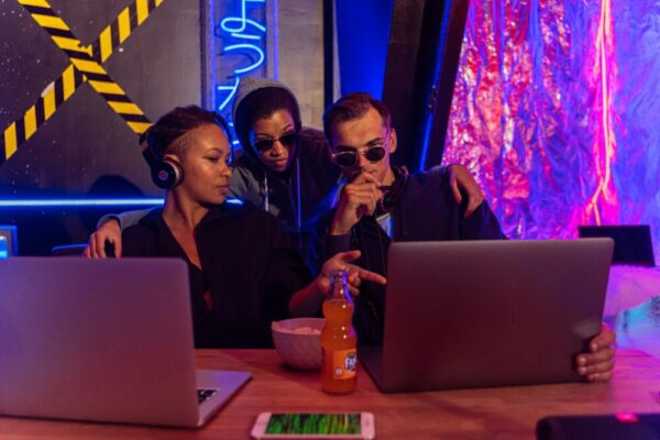 PDF與Office文件整理:雲端版本控管實用指南 Three people collaborate on laptops in a cyber-themed workspace, discussing strategies.
