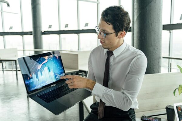 A businessman in an office analyzing market trends on a laptop with graphs and charts displayed.