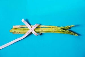 Fresh asparagus wrapped with measuring tape on a vibrant blue background.