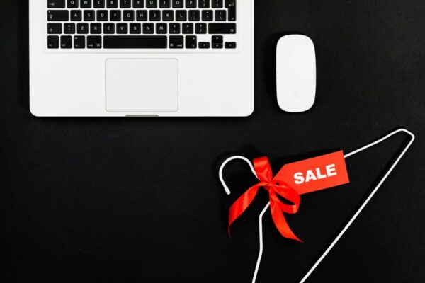 電商加購功能設計指南:提升銷售的實用步驟 Stylish flat lay of a laptop, mouse, and sale tag on a hanger for online shopping concept.