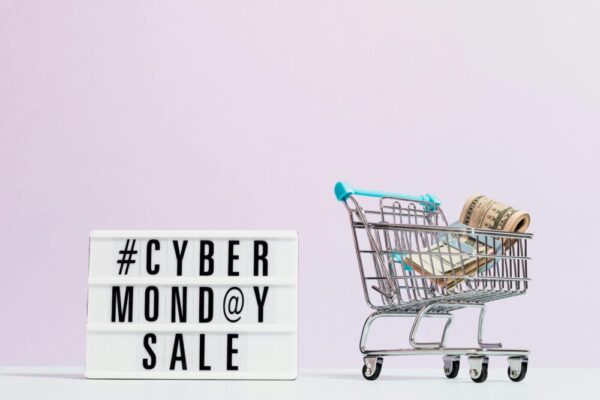 電商折扣設計秘訣:不損品牌價值的促銷策略 Shopping cart filled with cash beside a Cyber Monday sale sign, perfect for retail promotions.
