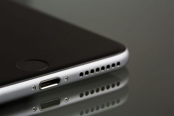 A sleek smartphone close-up highlighting its lightning connector and speaker, reflecting on a surface.