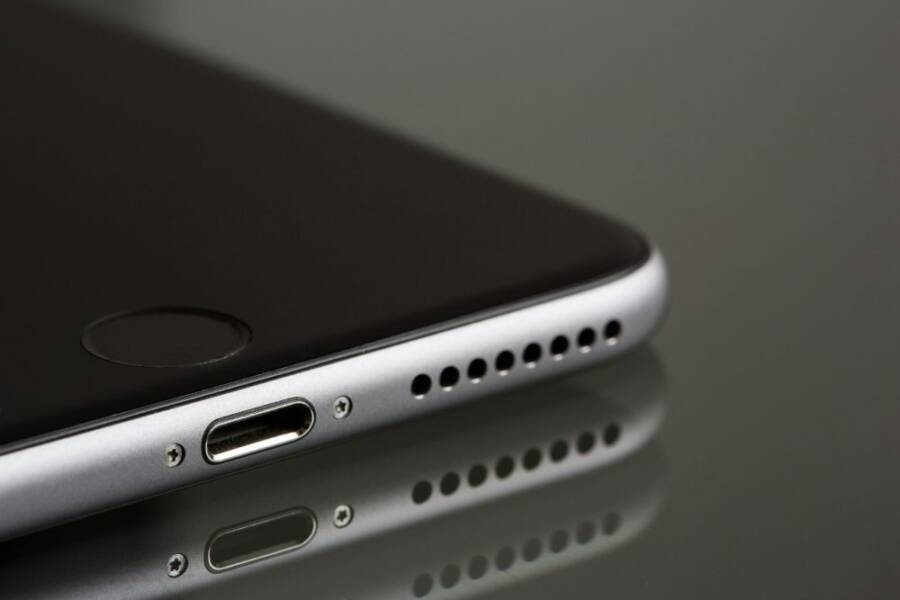 A sleek smartphone close-up highlighting its lightning connector and speaker, reflecting on a surface.