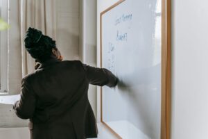 Rear view of a professional woman writing on a classroom whiteboard, focusing on lecture preparation.