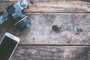 A vintage camera and smartphone on a rustic wooden surface, highlighting technology contrast