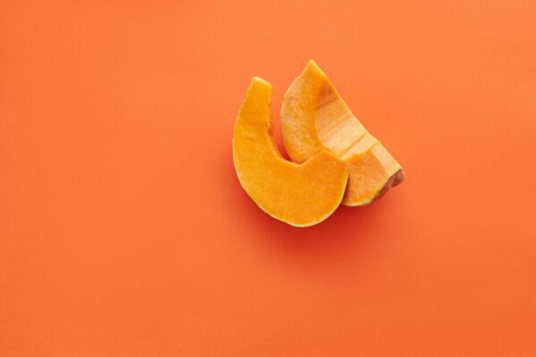Top view of fresh pumpkin slices on a vibrant orange background, highlighting fall produce.