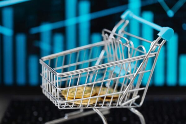 如何設計高轉換購物流程?電商銷售實用指南 A miniature shopping cart filled with coins against a digital financial graph background.