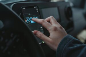 Hand interacting with GPS navigation on a smartphone mounted in a car interior.