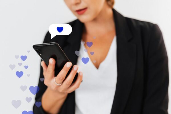 Close-up of a woman holding a smartphone with floating heart icons, illustrating digital engagement.