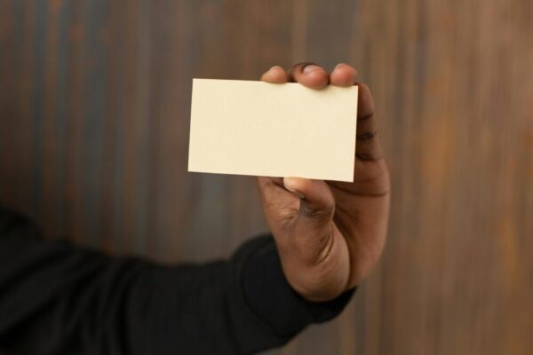 A close-up shot of an unrecognizable man holding a blank business card against a wooden background.