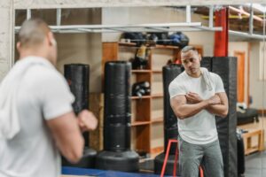 健美練習結合內在對話:提升動機與表現的實用指南 A muscular man stands in front of a gym mirror, reflecting on his progress during an intense workout session.