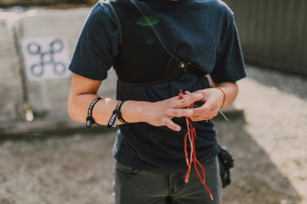 A young archer adjusts wristbands and equipment outdoors, preparing for archery practice on a sunny day.