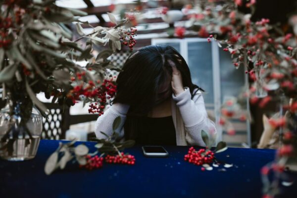 Woman in despair at table with red berries and smartphone, hands on head
