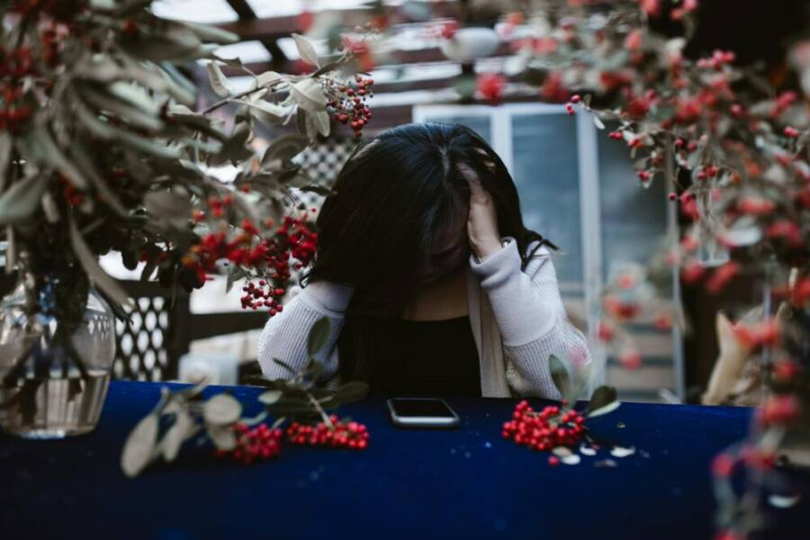 Woman in despair at table with red berries and smartphone, hands on head