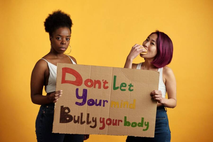 Two diverse women with empowering message against body shaming on a yellow background.