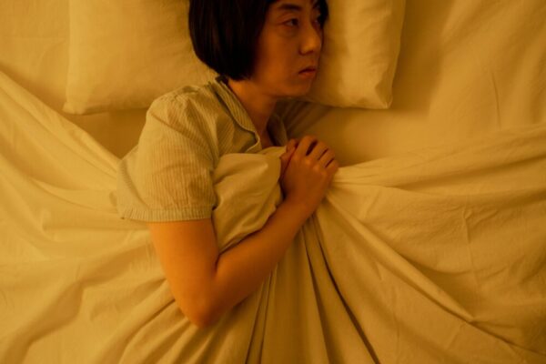 Side view of an Asian woman lying in bed, reflecting anxiety and insomnia in dim light.