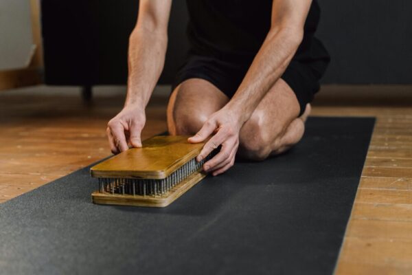 A man sets up a wooden meditation board on a yoga mat indoors, highlighting mindfulness practice.