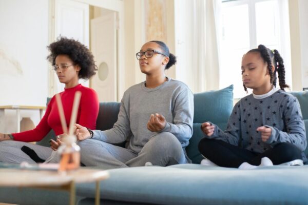 A family of three meditates together on a living room couch, promoting mindfulness.