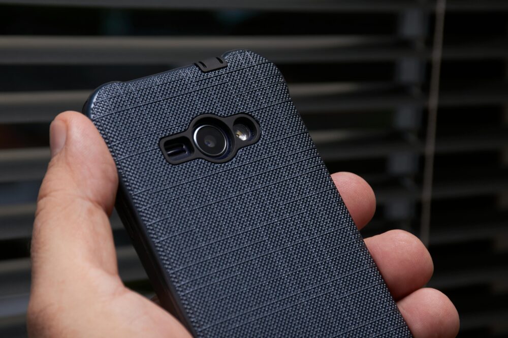 A close-up of a hand holding a smartphone with a textured blue case near a window, showcasing modern technology.